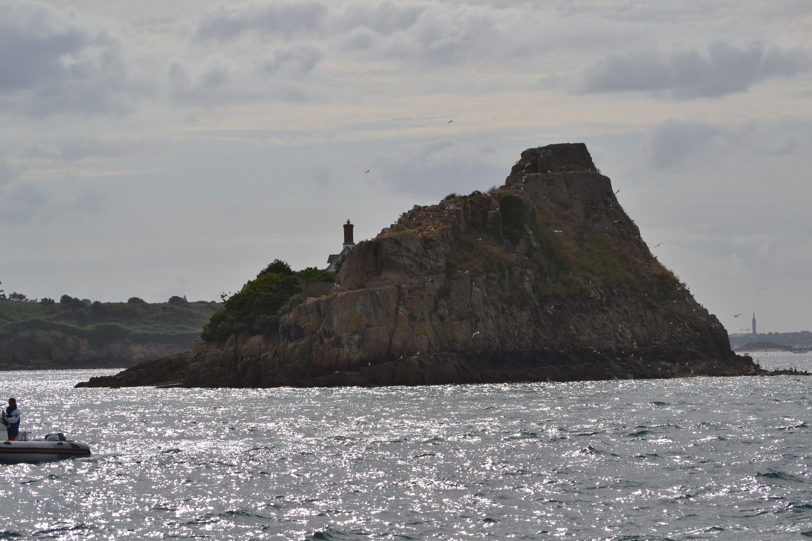 Un'isola rocciosa con un faro all'orizzonte, circondata dall'acqua.