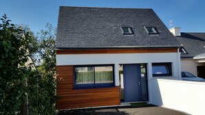 Ein modernes, zweistöckiges Haus mit dunklem Dach, Holzfassade und weißer Außenwand.