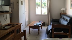 Una habitación pequeña y bien iluminada con una mesa de madera, un sofá de cuero, un televisor en la pared y una ventana con cortinas.
