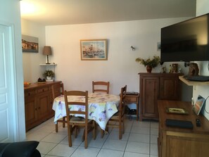 Una cocina compacta con una mesa, sillas, armarios de madera, un televisor y un cuadro en la pared.
