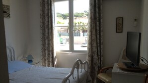 Un dormitorio con una cama, una silla, un escritorio con televisor y una ventana con cortinas.
