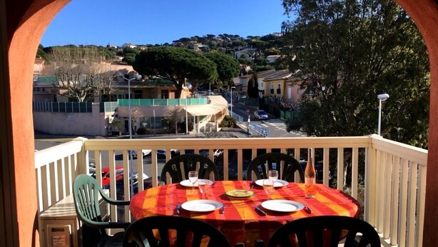 Un balcón con una mesa preparada para dos personas, con vista a una zona residencial con casas y árboles.