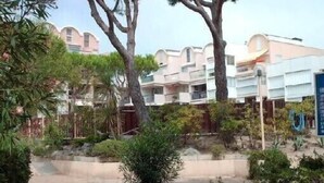 A hotel courtyard with a swimming pool, surrounded by trees and plants, and buildings in the background. - Grand T3 luxury duplex in highly sought after residence (Gruissan)
