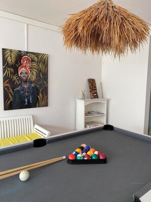 Relax in a cozy space with a pool table, a shelf filled with books and decorative items, and a unique ceiling lamp.