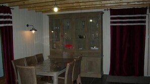 A dining area with a wooden table and chairs, a cabinet with glass doors, and red curtains.