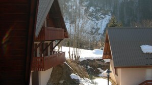 A wooden cabin with a balcony, a snow-covered landscape, and a mountain in the background.