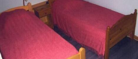 Una habitación pequeña con dos camas de madera, cada una con una manta roja. Hay dos mesitas de noche con lámparas.