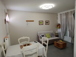 Een woonkamer met een eettafel, stoelen, een bank, een houten salontafel en een plafondventilator.