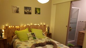 A bedroom with a bed, nightstands, a headboard with string lights, a shower, and a door. - Cozy vacation rental in the Arcachon Basin for 2–3 people: peaceful setting, amenities, and beaches (Gujan-Mestras)