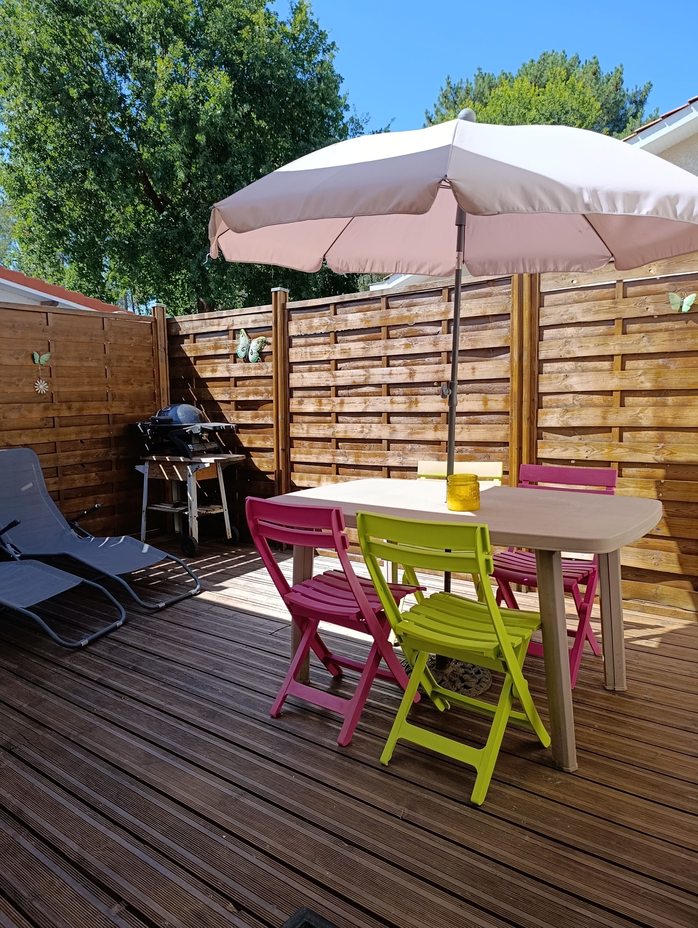 A wooden deck with a table and chairs, a grill, and an umbrella.