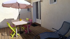 An outdoor patio with a table, chairs, an umbrella, and a door. - Cozy vacation rental in the Arcachon Basin for 2–3 people: peaceful setting, amenities, and beaches (Gujan-Mestras)