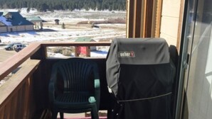 Een balkon met uitzicht op een besneeuwd landschap, een barbecue en een overdekte stoel.