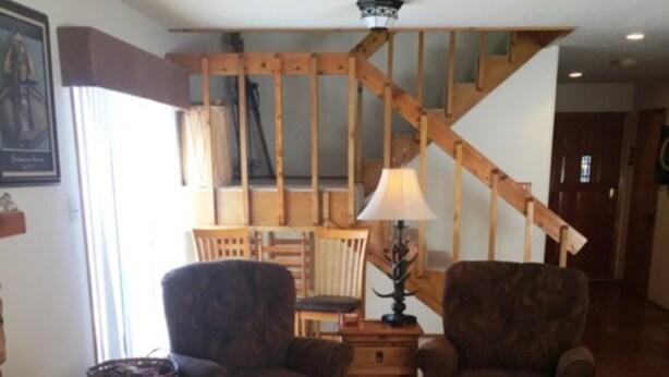 Een woonkamer met twee fauteuils, een houten trap en een betegelde vloer.