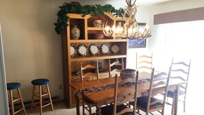 Een eetgedeelte met een houten tafel en stoelen, een boekenplank met decoratieve borden en een kroonluchter.