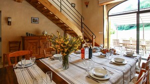 A dining area with a table set for four, a wooden staircase, and a view through large windows. - Charming 4-star Gite with pool (Capdrot)