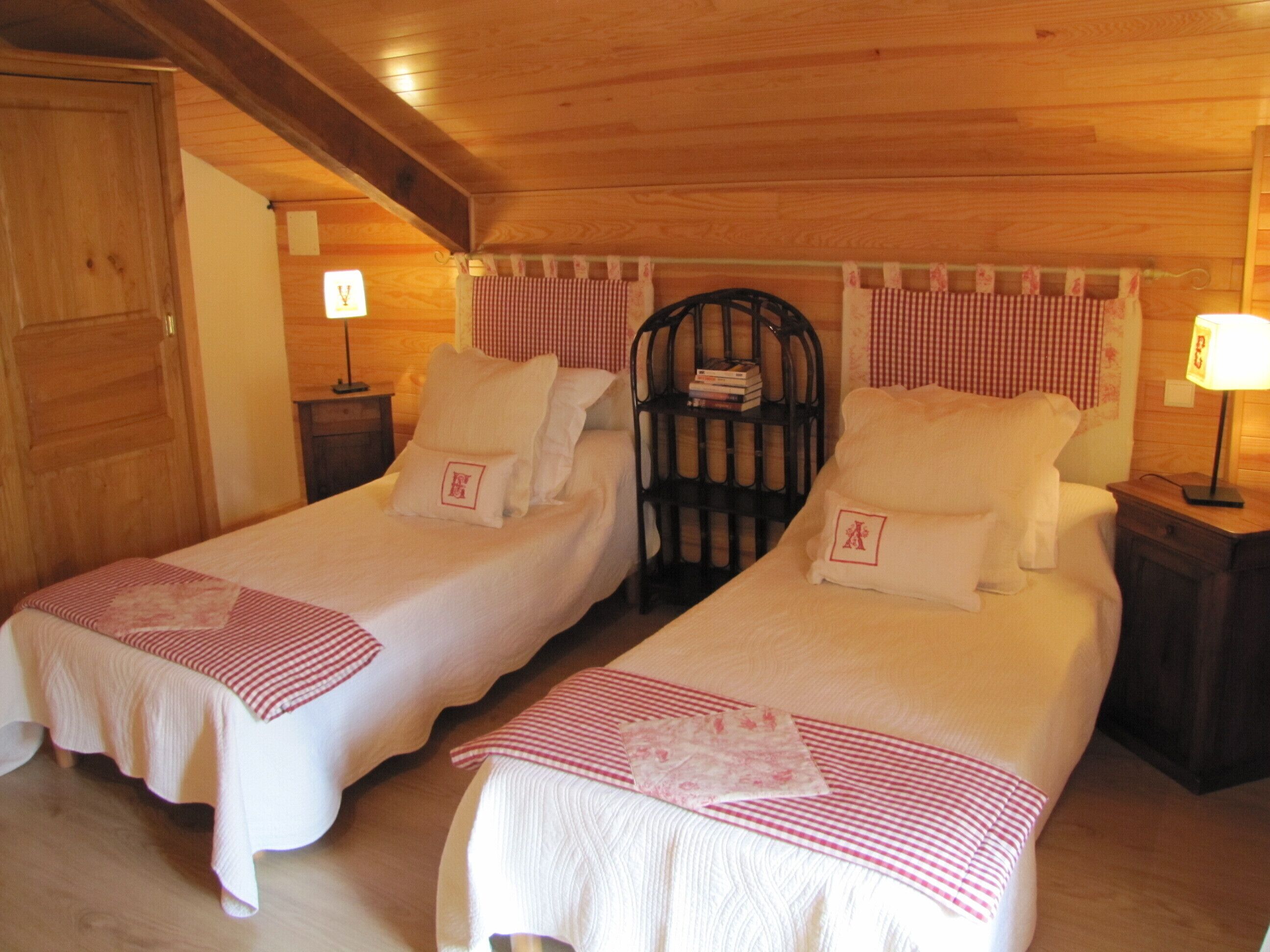 Two single beds with matching headboards and footboards, a wooden ceiling, and a small bedside table with a lamp.