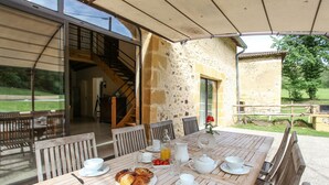 An outdoor dining area with a wooden table set for breakfast, including croissants, fruit, and beverages. - Charming 4-star Gite with pool (Capdrot)