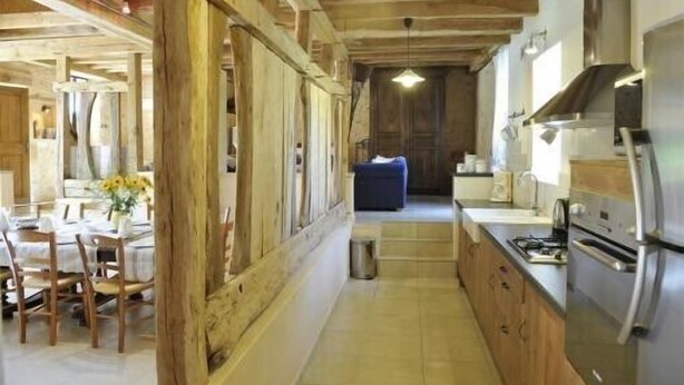 A narrow kitchen with wooden beams, a dining area with a table and chairs, and a blue sofa in the background. - Charming 4-star Gite with pool (Capdrot)