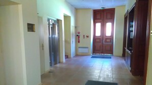 Un couloir avec un sol carrel é, une porte en bois au fond et un extincteur accroché au mur.