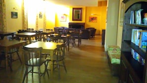 Une pièce chaleureuse avec une cheminée, une bibliothèque et un coin repas comprenant des tables et des chaises.