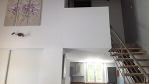 Un escalier menant à l’étage supérieur, une porte blanche et un mur orné d’un tableau représentant des motifs floraux.