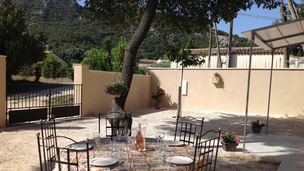 Un espace de restauration en plein air avec une table ronde et des chaises, entouré d’une terrasse en gravier et d’un petit muret.