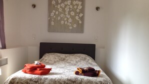 Un lit bien fait, recouvert d’une couvre-lit à motifs floraux, avec deux serviettes pliées et un luminaire fixé au mur.