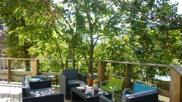 An outdoor deck with wicker furniture, a table with drinks, and a view of trees and a body of water. - Country house with large garden and swimming pool (Carces)