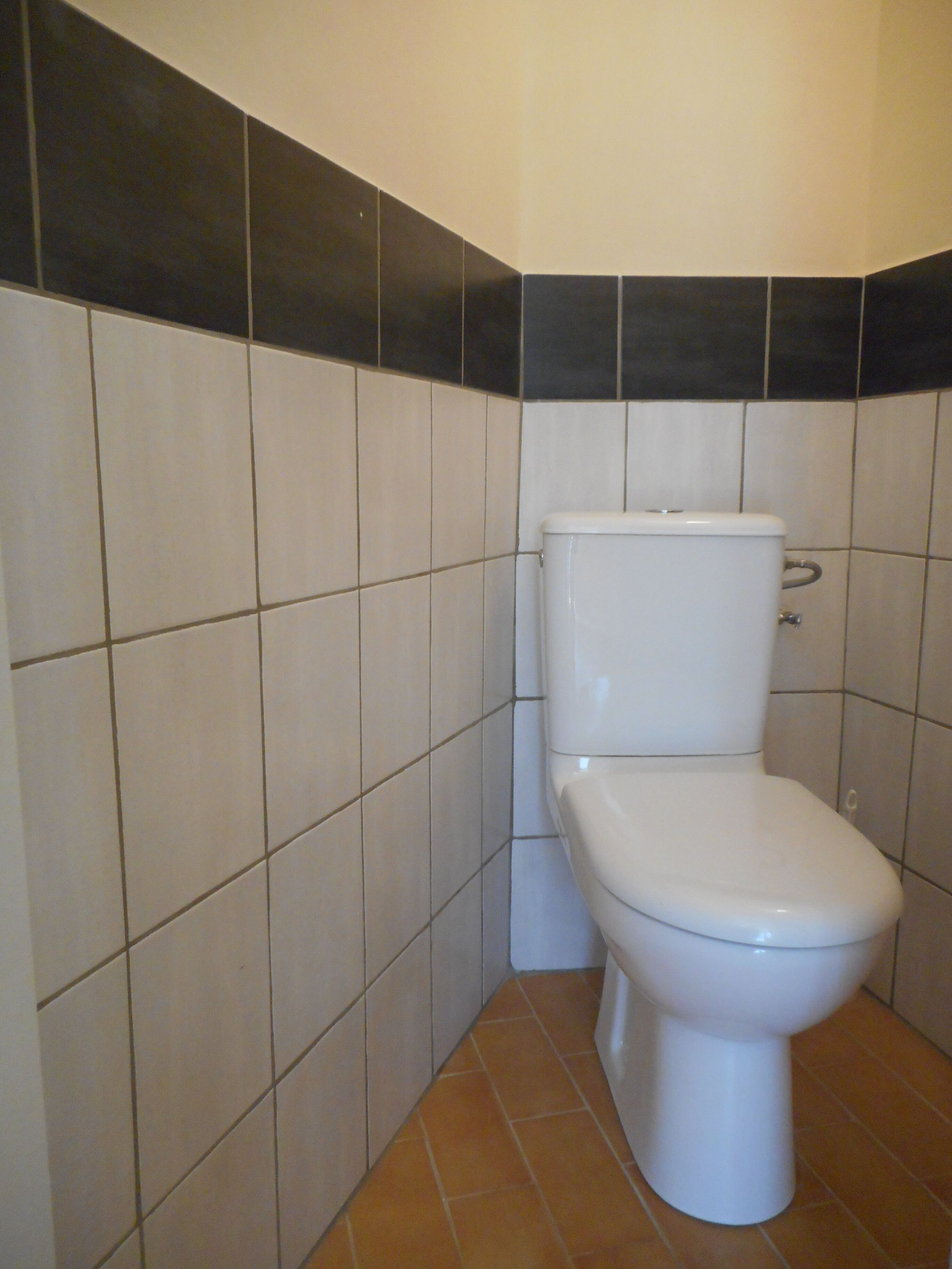 Ein Badezimmer mit Toilette, gefliesten Wänden und einem gefliesten Boden.