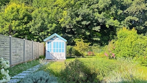 A small blue and white shed with a wooden deck in a lush garden. - Charming cottage with bay view and garden (Saint-Valery-Sur-Somme)
