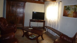 A living room with a wooden ceiling, a television on a stand, leather chairs, a coffee table, and a painting on the wall. - A gîte of character and grand comfort in the heart of nature  3*** (St Laurent le Minier)