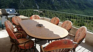 A round table with six chairs, a grill, and a view of a mountainous landscape. - A gîte of character and grand comfort in the heart of nature  3*** (St Laurent le Minier)