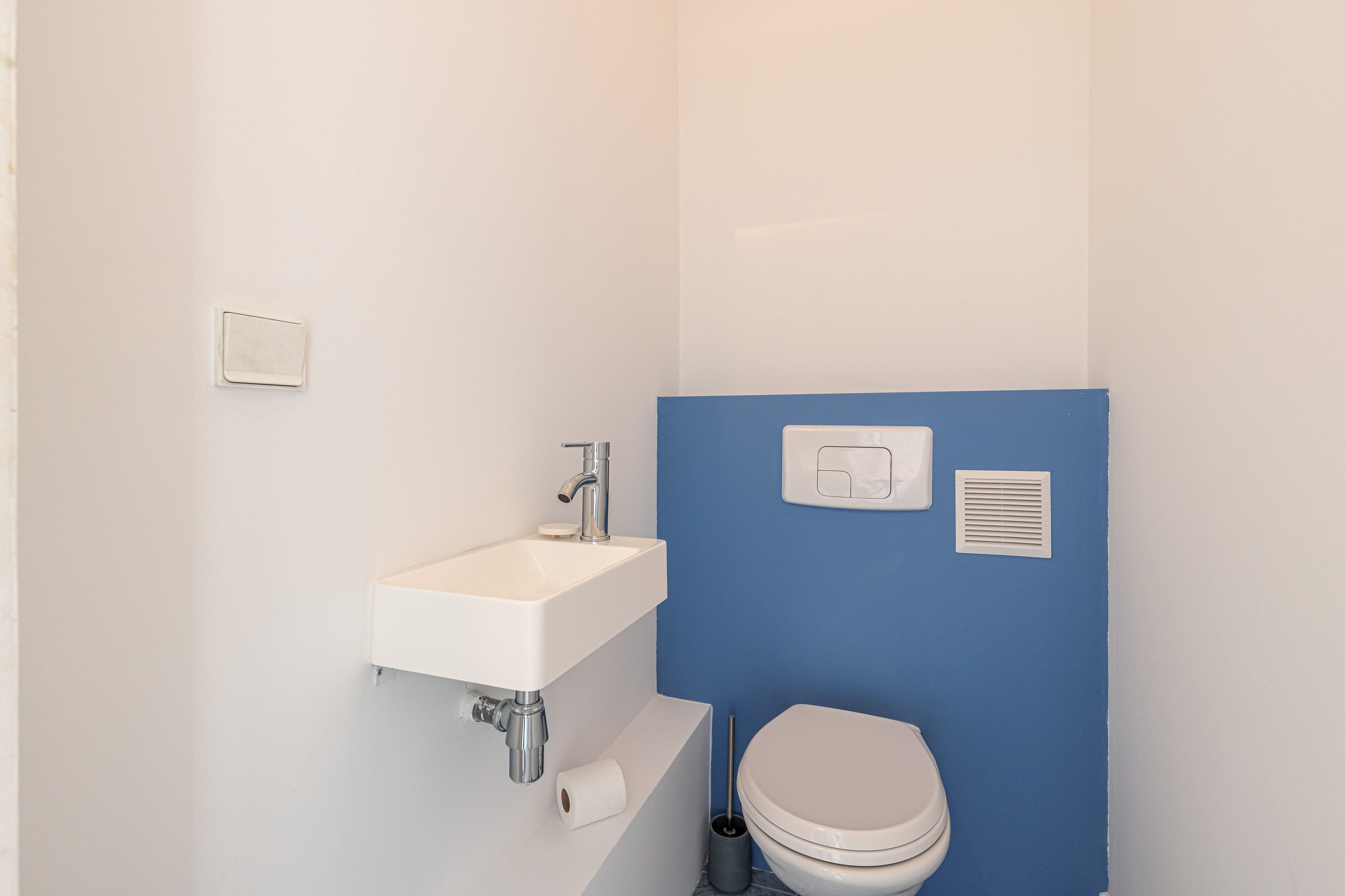 Une salle de bain avec un lavabo blanc, des toilettes et un mur d’accent bleu.