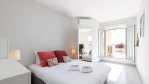 Quarto moderno com cama, mesa de cabeceira e vista para o pátio externo.