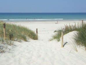 Un camí de sorra que condueix a l'oceà, amb ones i persones al lluny.