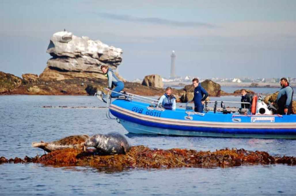 A boat with people on it near rocky shores and a lighthouse in the background.