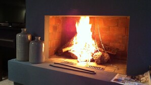 Een haard met een vlammend vuur, een flatscreen televisie erboven en twee metalen bakken op de schoorsteenmantel.