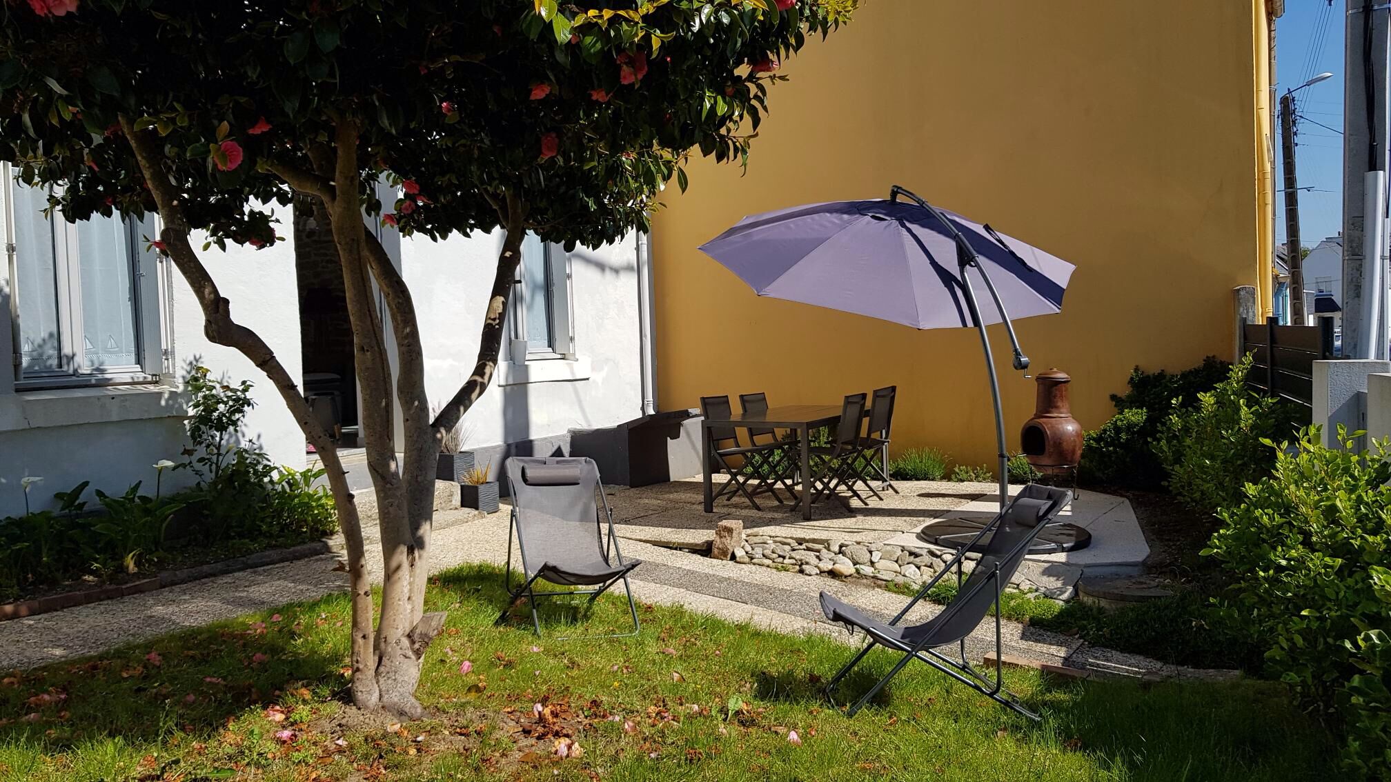 Un espace extérieur aménagé avec une table et des chaises, un grand parasol et un pot décoratif.