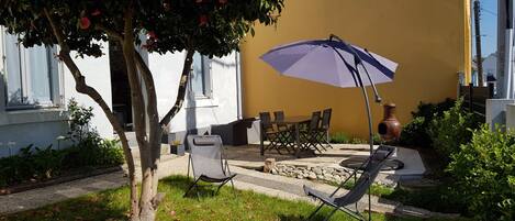 Un espace extérieur aménagé avec une table et des chaises, un grand parasol et un pot décoratif.