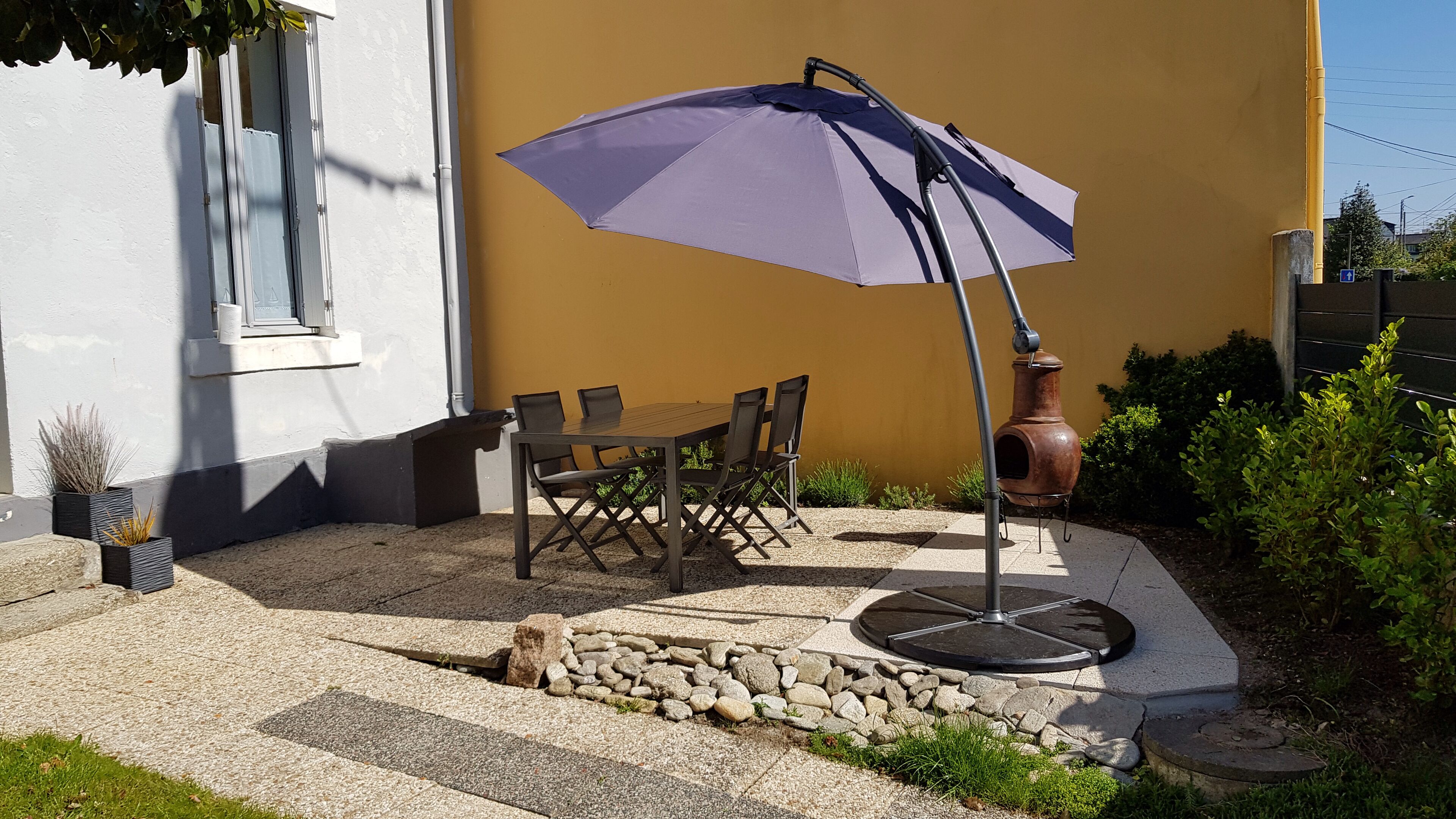 An outdoor patio with a table and chairs, a purple umbrella, and a large ceramic pot.