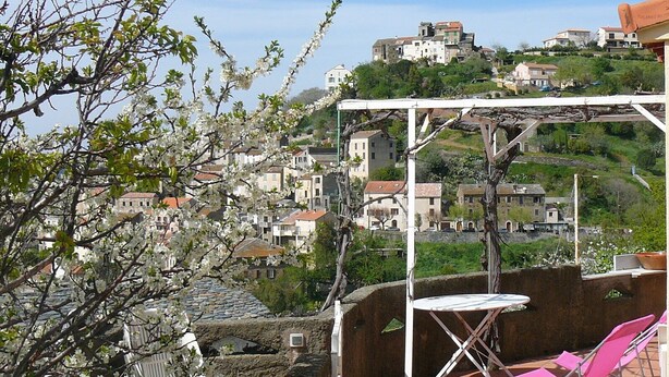 A terrace with a table and chairs, overlooking a hillside village with traditional buildings. - Sunny villa with stunning views over the village and the sea (Oletta)
