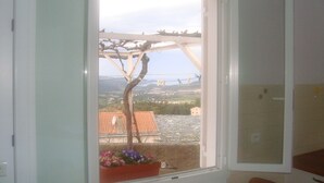 A room with a large window, a potted plant, and a view of a bridge and landscape. - Sunny villa with stunning views over the village and the sea (Oletta)
