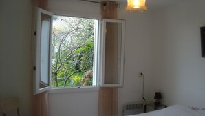 A bedroom with a bed, a chair, a window with curtains, a wall-mounted lamp, and a radiator. - Sunny villa with stunning views over the village and the sea (Oletta)