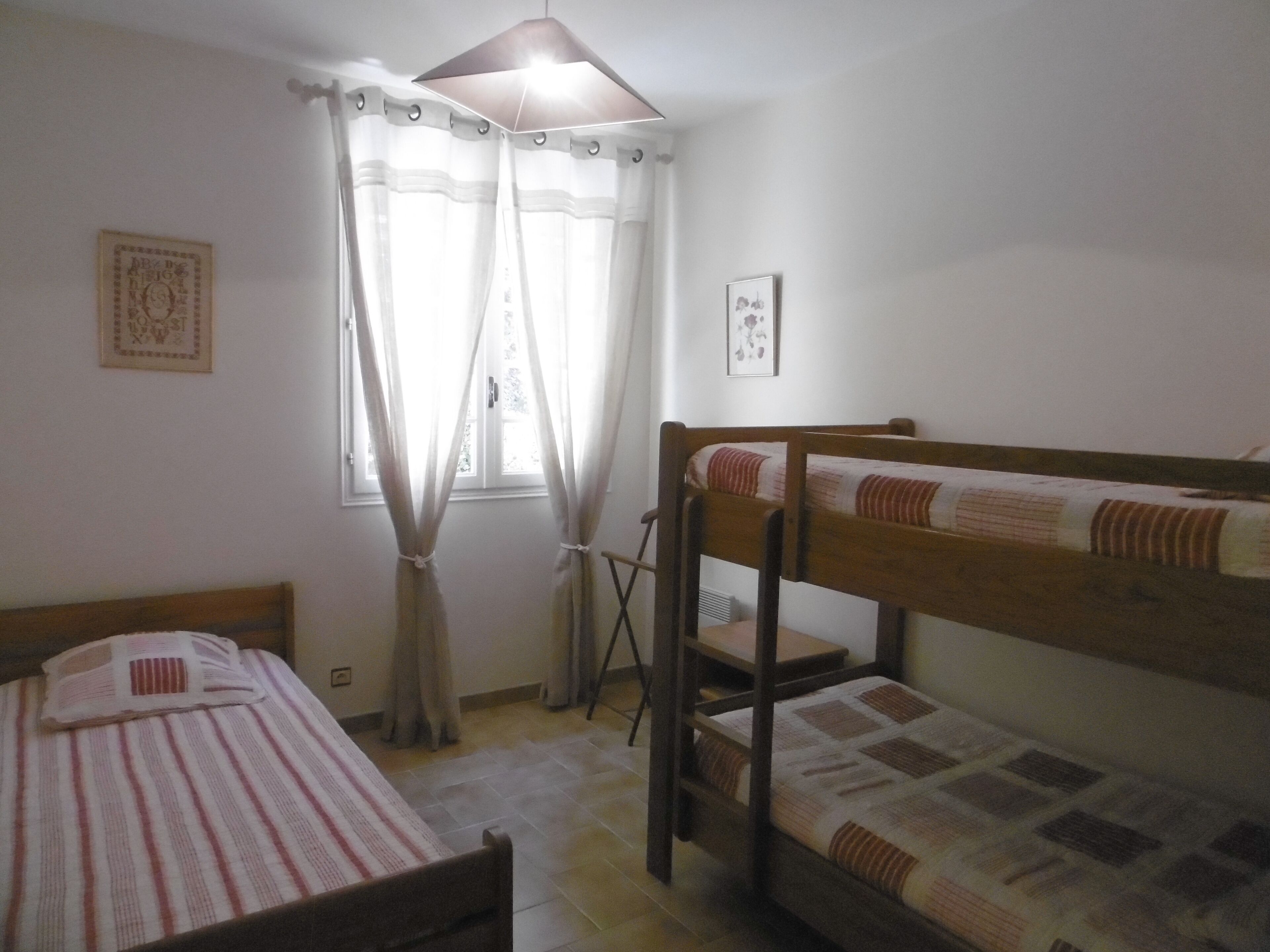 Un dormitorio con dos literas, una ventana con cortinas translúcidas y una pequeña escalera.