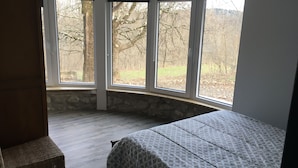 Une chambre avec une grande fenêtre, un lit et une chaise.