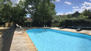 Une piscine rectangulaire dotée d’une terrasse en bois, entourée d’une clôture et d’arbres.