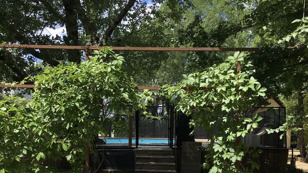 Une terrasse en bois menant à une zone de piscine, entourée de murs en pierre et de verdure.