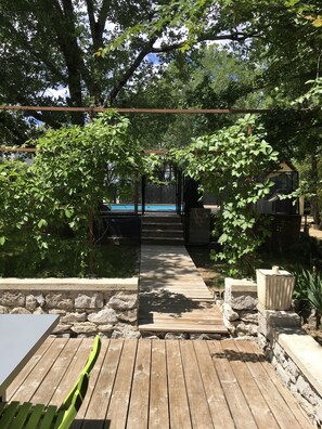 Ett trädäck som leder till ett poolområde, omgivet av stenmurar och grönska.
