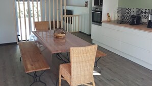 Une cuisine moderne avec un coin repas, comprenant une table et des chaises en bois, un luminaire suspendu et une vue dégagée sur l’extérieur grâce à une grande fenêtre.