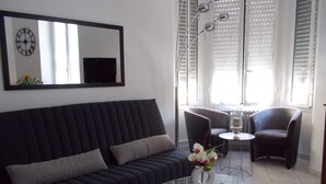 A modern living room with a dark sofa, a glass coffee table, and two armchairs.